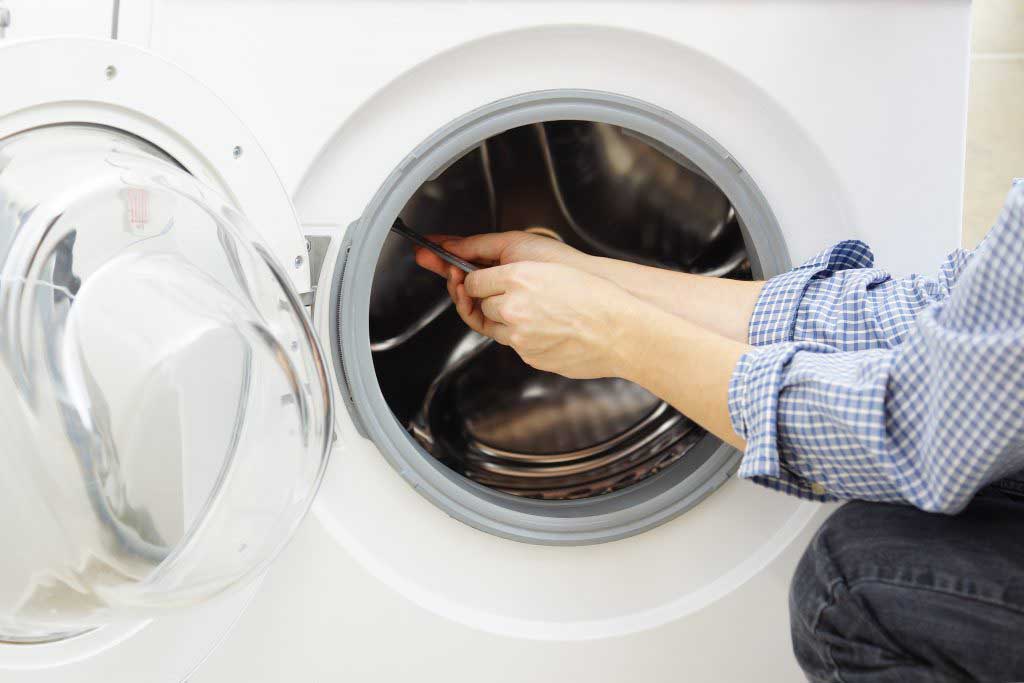 A man in a blue shirt repairing a washer/dryer