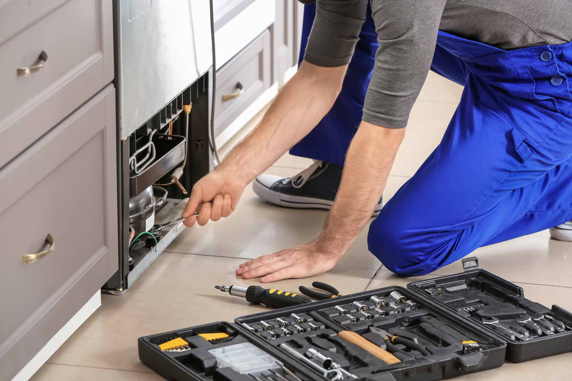 Appliance repair technician kneeling to repair a refrigerator