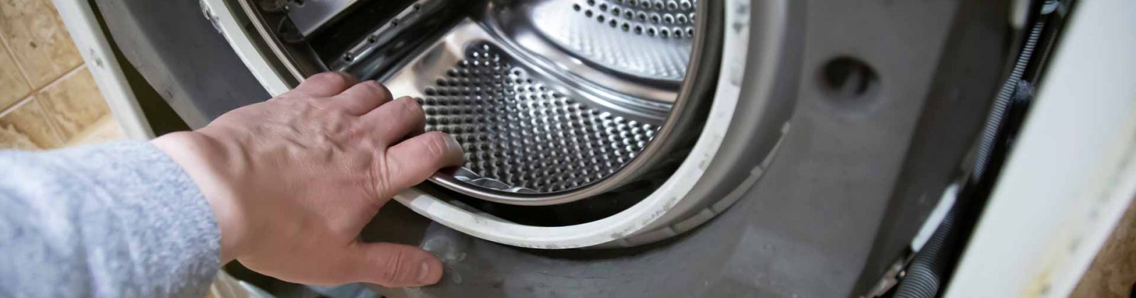 Hand of appliance repair technician reaching in to washer/dryer drum
