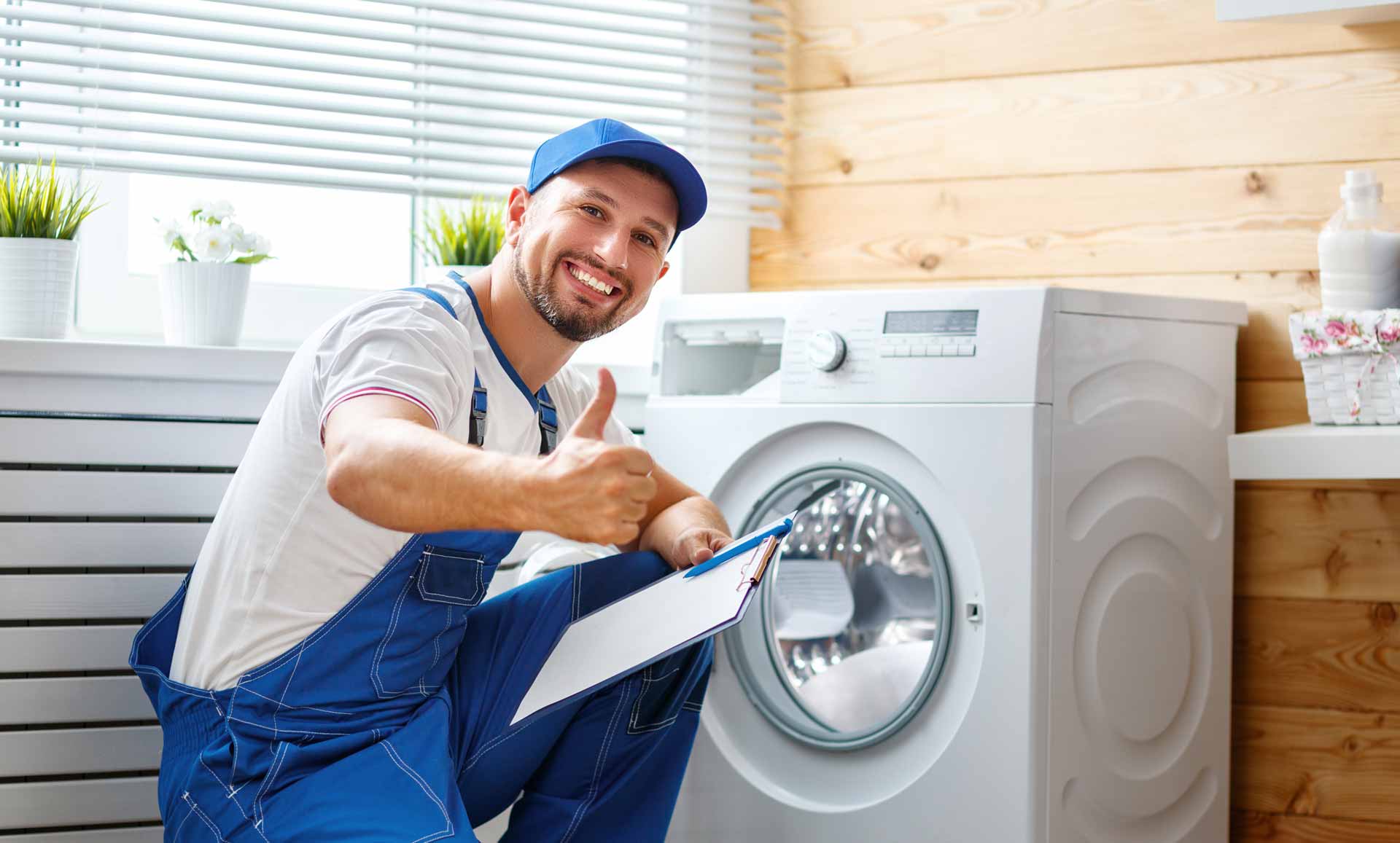Appliance repair technician posing with a washer/dryer. He is smiling and giving the camera a "thumbs up" gesture